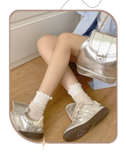 Dettaglio di sneaker metallizzate argento con calze a balze su pavimento in legno