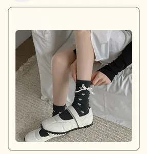 Détail de chaussettes mi-mollet gris foncé avec cœurs blancs et nœuds style ballerine