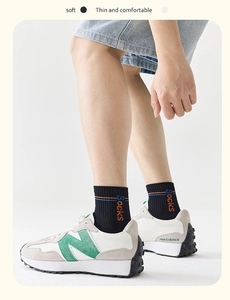 Dettaglio di sneaker bianche e grigie con logo N verde e calze nere con scritte moda