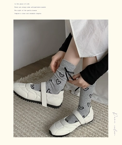 Détail de chaussettes grises avec motif cœur noir et nœuds en satin et souliers blancs