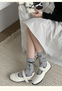 Détail de chaussettes grises style ballet avec motifs de cœurs noirs et nœuds délicats