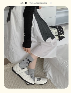 Détail de chaussettes grises à cœurs avec nœuds noirs et chaussures Mary Jane blanches
