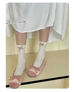 Detail of white lace mid-calf socks with pink bows paired with soft pink ballet flats