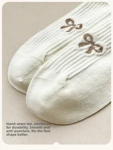 Macro detail of white ribbed socks featuring premium knit and brown bow embroidery