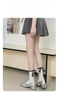 Detail of white mid-calf socks with black ruffle trim and decorative satin bows