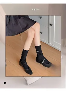 Detail of black ribbed cotton socks featuring delicate white bow embroidery and Mary Jane shoes