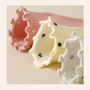 Detail of ruffled cuffs on polka dot knit socks in pink, yellow and beige tones
