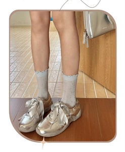Detailed view of hollow bow pattern socks worn with metallic silver sneakers and ribbon laces