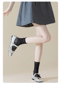Detail of sheer black lace socks paired with silver metallic Mary Jane shoes and pearls