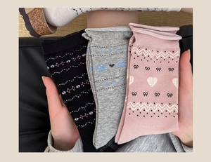 Detail of knitted mid-calf socks with heart and bow patterns in black, grey, and pink