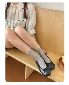 Detail of grey ruffled knit mid-calf socks paired with black bow ballet flat shoes