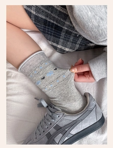 Detail of high-stretch grey crew socks with blue bows and black hearts on a soft bed