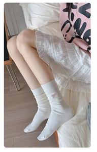 Detail of white ribbed crew socks featuring delicate pink embroidered bow accents