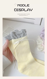 Close-up of yellow knit sock featuring a grey ruffled edge and delicate white ribbon bow