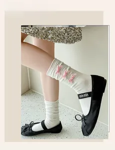 Close-up of white mid-calf socks featuring pink velvet bows and black ballet flats