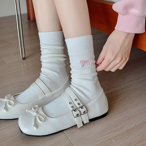 White rib-knit crew socks with pink embroidered bow accents worn with Mary Jane shoes