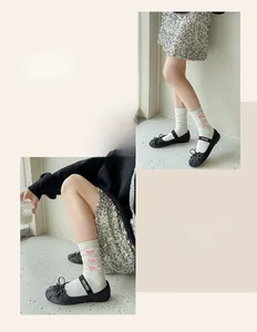 Detail of white mid-calf socks with pink velvet bows and black Mary Jane shoes