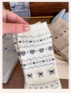 Macro detail of knit crew socks featuring heart and bow patterns in soft cream and gray