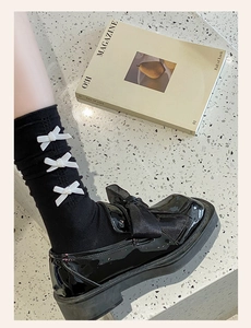 Detail of black knit calf socks with white satin bows paired with patent loafers