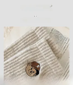 Detailed close-up of thick beige wool sock featuring a cute brown bear embroidery