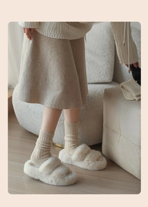 Ciabatte di peluche beige e calze spesse in cotone a coste in un ambiente accogliente