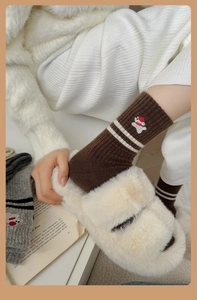 Close-up of thick wool socks featuring striped cuffs and a cute small bear embroidery