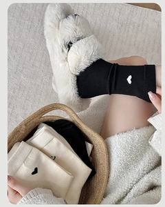 Dettaglio di calze di cashmere nere e beige con ricamo a cuore in ambiente accogliente
