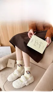 Detail of warm coral fleece socks with cute bear embroidery and white plush home slippers
