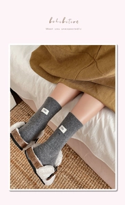 Close-up of dark grey knit socks with egg cloth label and plush slippers on a rug