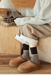 Cozy winter outfit featuring warm wool striped socks and brown plush slippers on a wooden floor