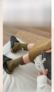 Close-up of knit crew socks in olive and grey with egg label detail and buckle mules