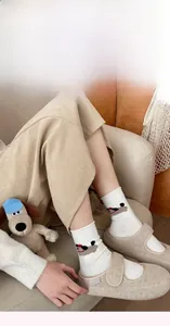 Detail of white cotton socks with cartoon dog embroidery and beige Mary Jane slippers