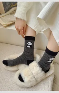 Detail of dark grey crew sock with panda embroidery paired with white plush slippers