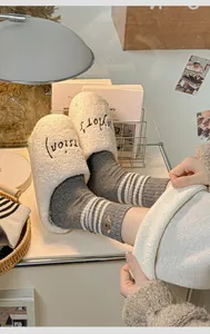 Detail of embroidered white sherpa slippers paired with grey striped wool socks
