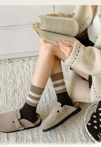 Detail of warm wool blend striped socks paired with suede clogs on a cozy rug