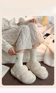 Detail of plush beige socks with bow embroidery and fuzzy winter slippers on a soft rug