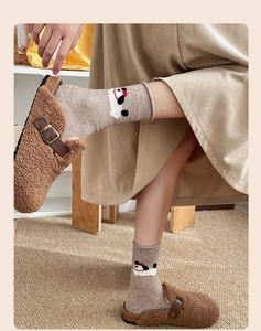 Close-up of brown plush mule slippers and cartoon dog pattern socks on a beige rug