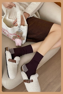 Détail de chaussettes côtelées café foncé à talon gris avec sabots en peau lainée blanche