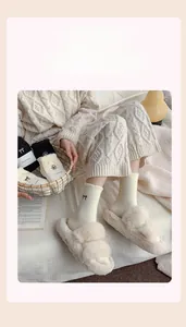 Close-up of thick winter socks with bow embroidery and cream plush slide slippers