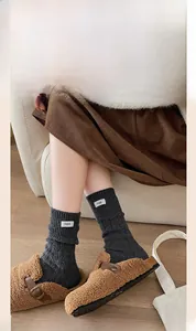 Detail of dark grey cable knit wool socks featuring a white egg label and plush slippers