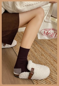 Détail de mules en peau de mouton avec bride en cuir marron et chaussettes en tricot