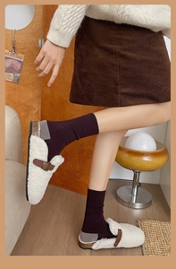 Détail de chaussettes en maille violet foncé avec mules en peau lainée blanche et jupe
