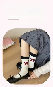 Close-up of cream crew socks featuring red bow prints and black double-layered cuffs