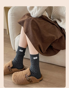 Detail of dark grey wool knit socks with 'egg' label and cable texture on feet
