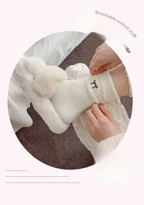 Close-up of white plush thermal socks with black bow embroidery and fuzzy slippers