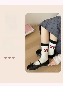 Detail of cream cotton crew socks with red bow pattern and black leather shoes