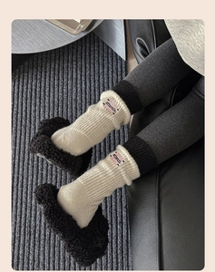 Detail of cream rib-knit mid-calf socks with black cuffs and pink attends letter patch