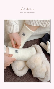 Detail of cream plush winter socks featuring black floral embroidery and fluffy texture