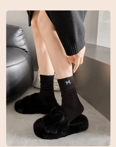 Detail of black crew socks with white bow embroidery paired with fluffy plush slippers
