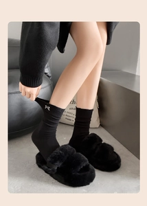 Close-up of black knit socks with delicate white bow embroidery and fuzzy slippers